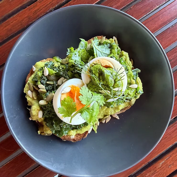Tartines d’avocat, œuf mollet, pesto, kale et graines de courge dans une assiette